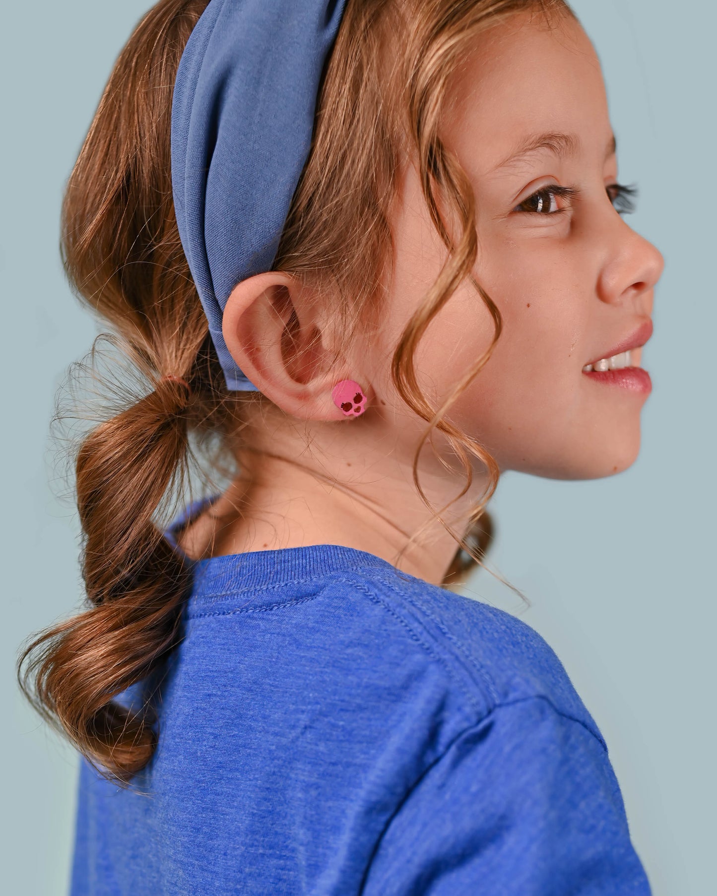 Close-up of a girl wearing pink skull stud earrings, complementing her blue top and headband with a subtle touch of playful edginess.