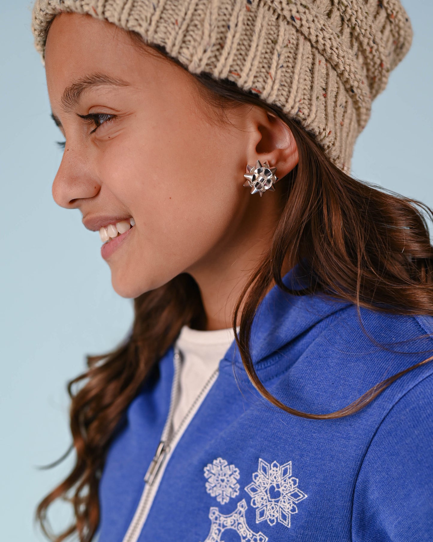 Close-up of a girl wearing silver Bow Earrings, complementing her casual winter attire with a knit hat.