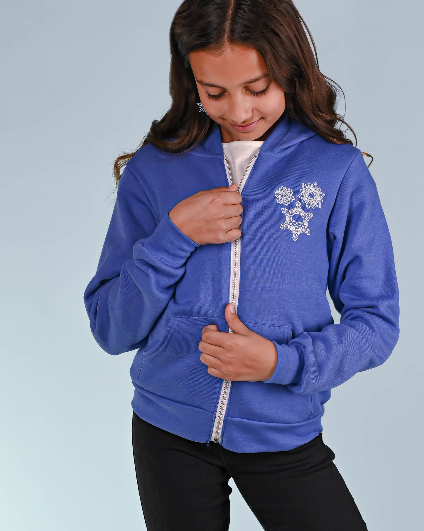 Youth in blue hoodie with intricate snowflake skull embroidery, offering a playful twist to winter wear.