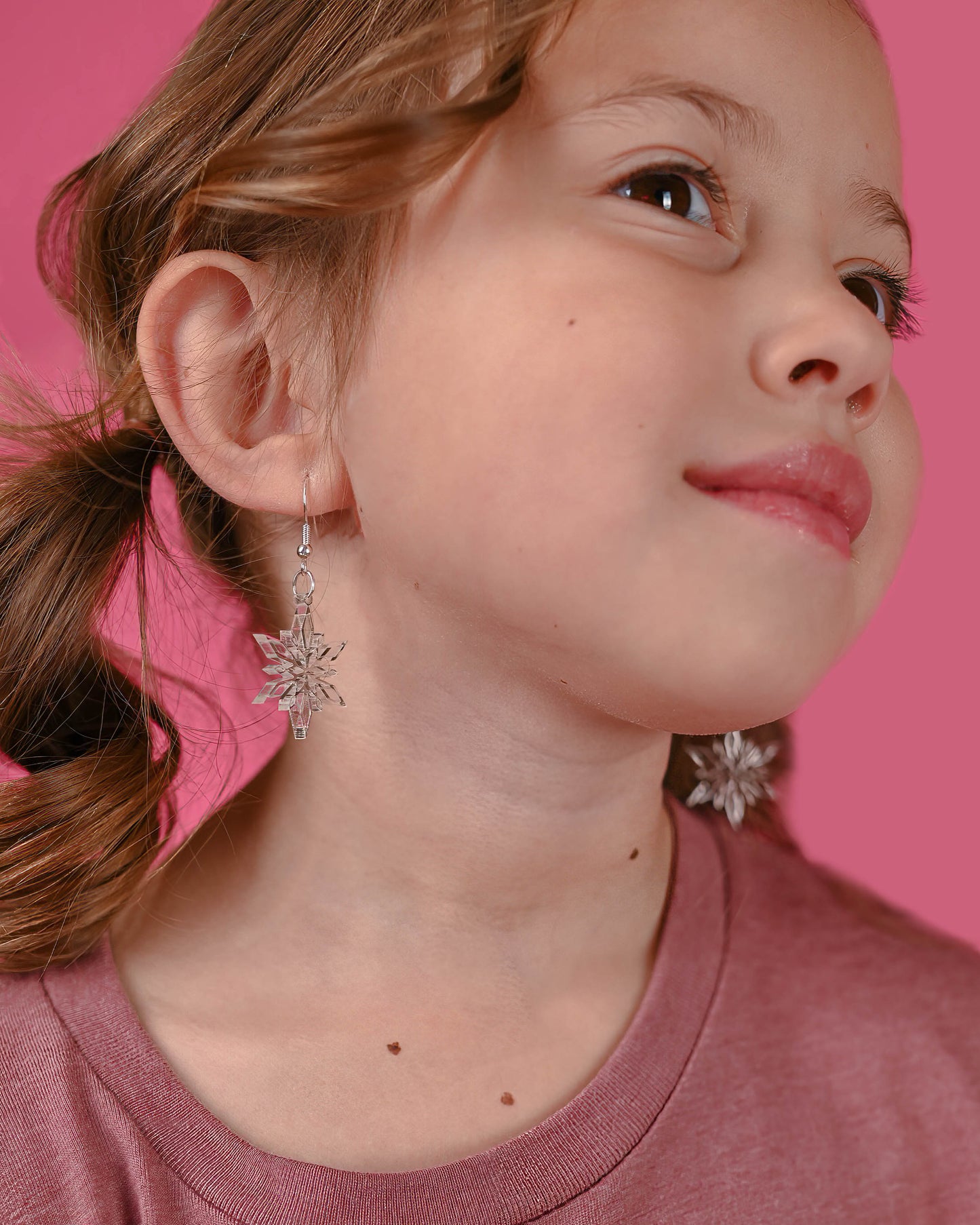 Happy young girl in a pink background sporting the clear snowflake earrings, adding a playful twist to her outfit.