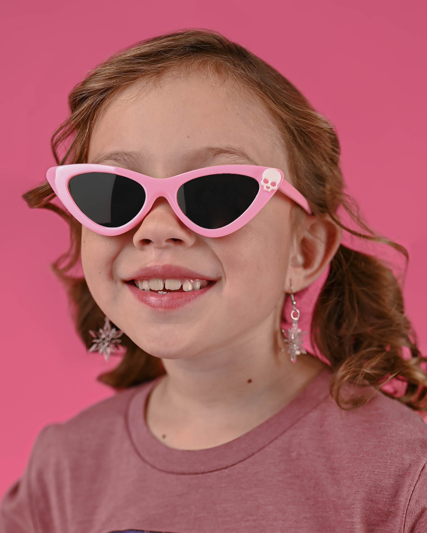 A cheerful young girl modeling Pink Skull Cat Eye Sunglasses, showcasing a playful fashion statement.