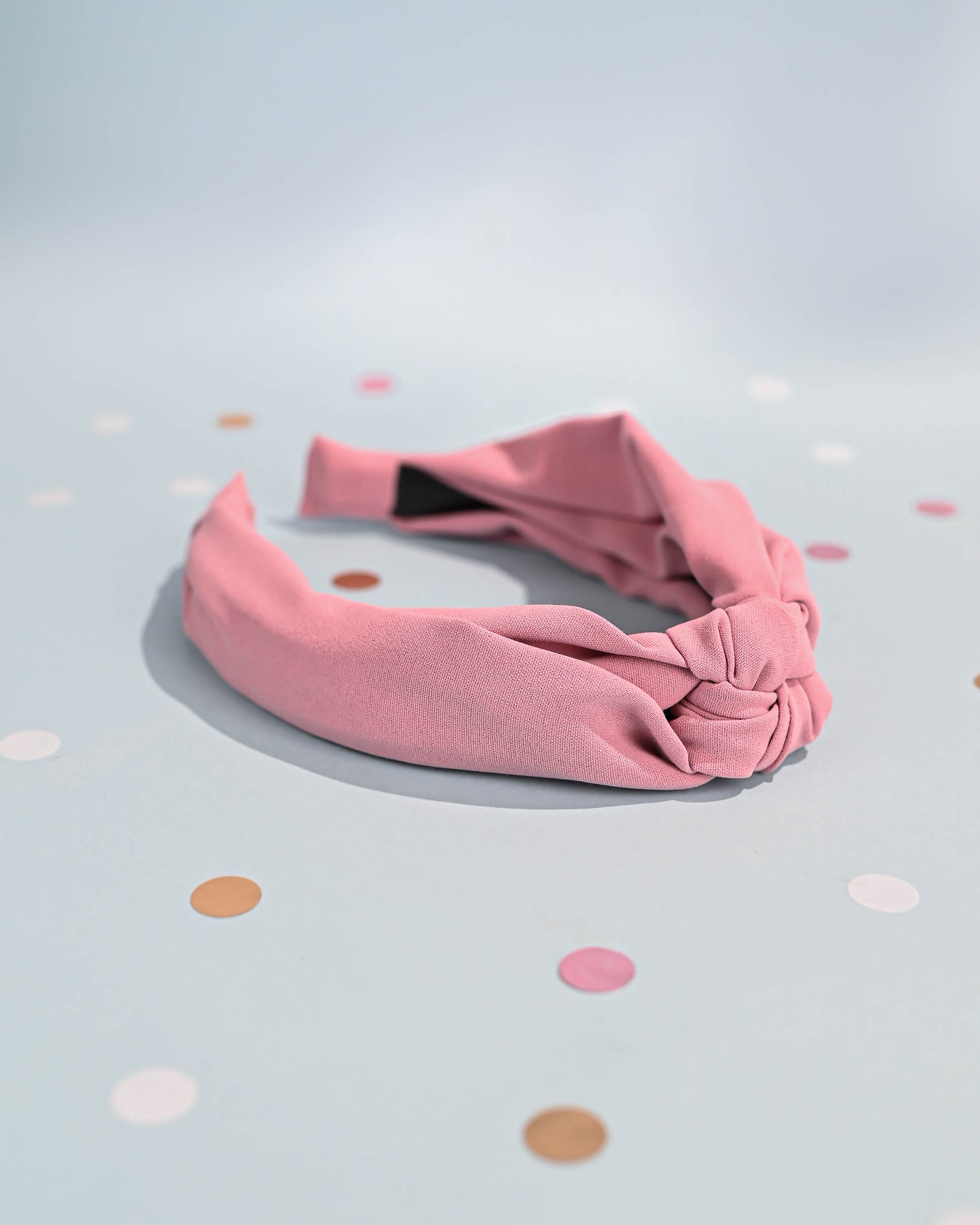 Pink top knot headband with a focus on the knot, polka dot background.