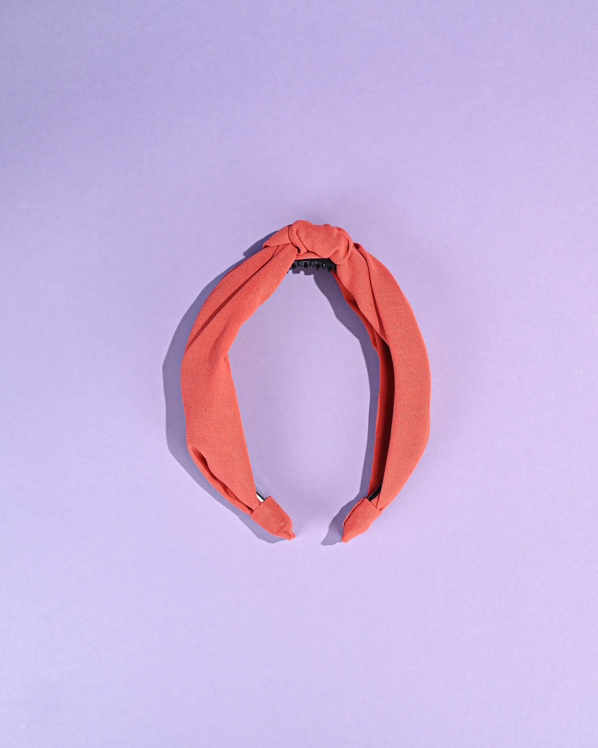 Coral top knot headband displayed on a purple background.