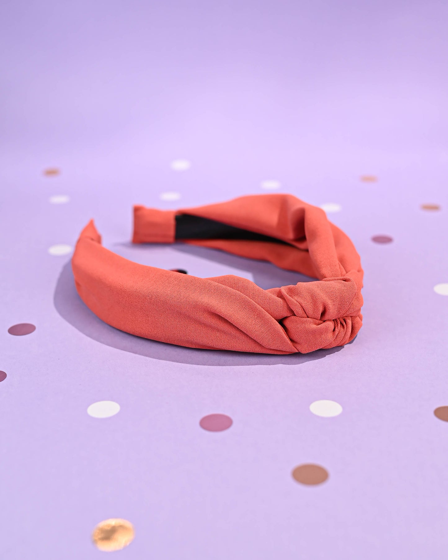 Coral top knot headband angled view on a polka dot background.