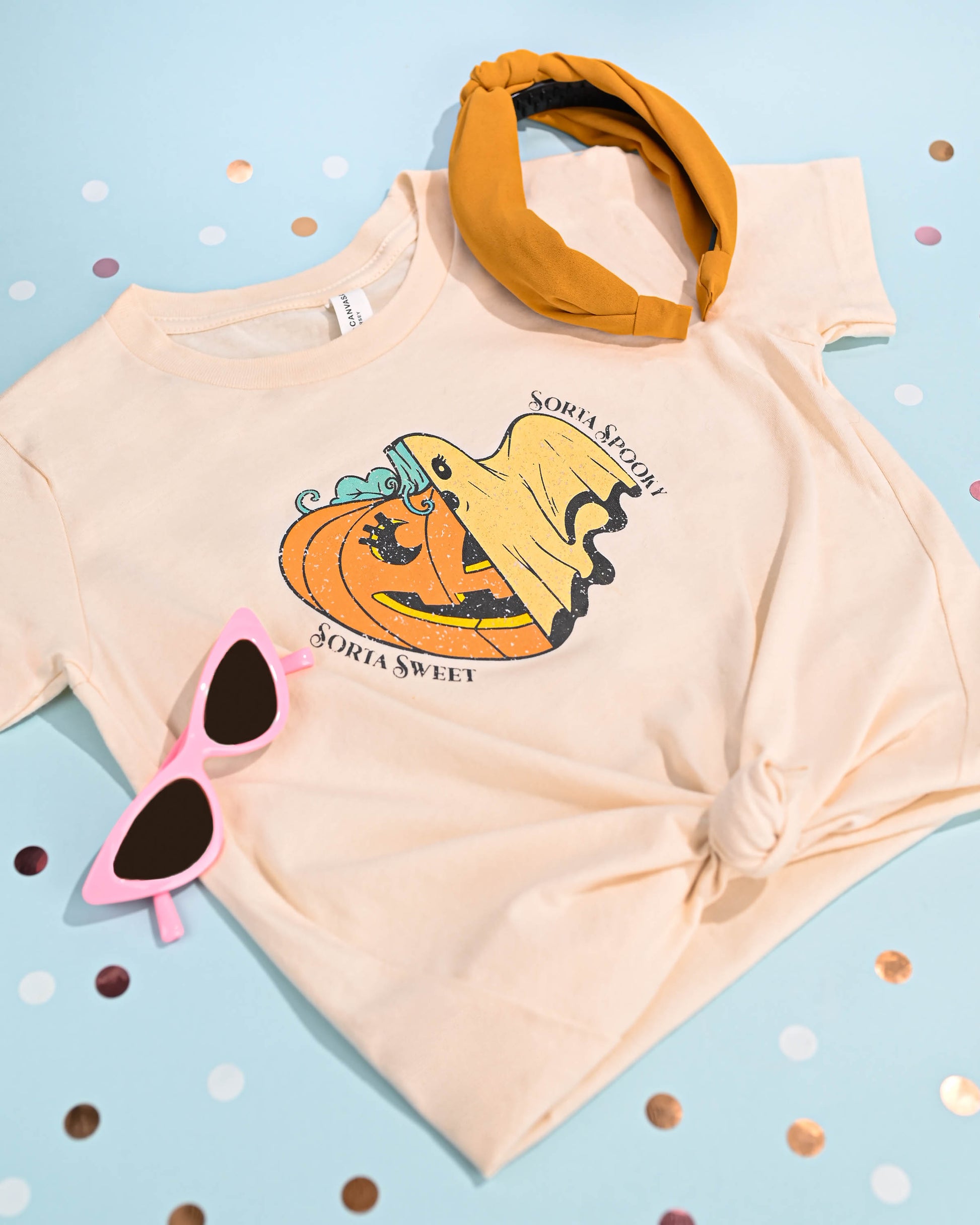 Playful Halloween-themed children's t-shirt laid out with accessories on a polka dot background.