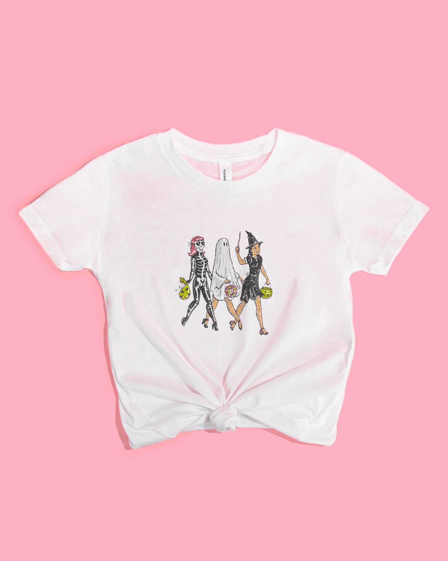 Happy Donut white Trick or Treaters T-shirt with a knotted waist, featuring a playful Halloween design with a skeleton, ghost, and witch on a pink background. Great non-costume Halloween outfit for girls.