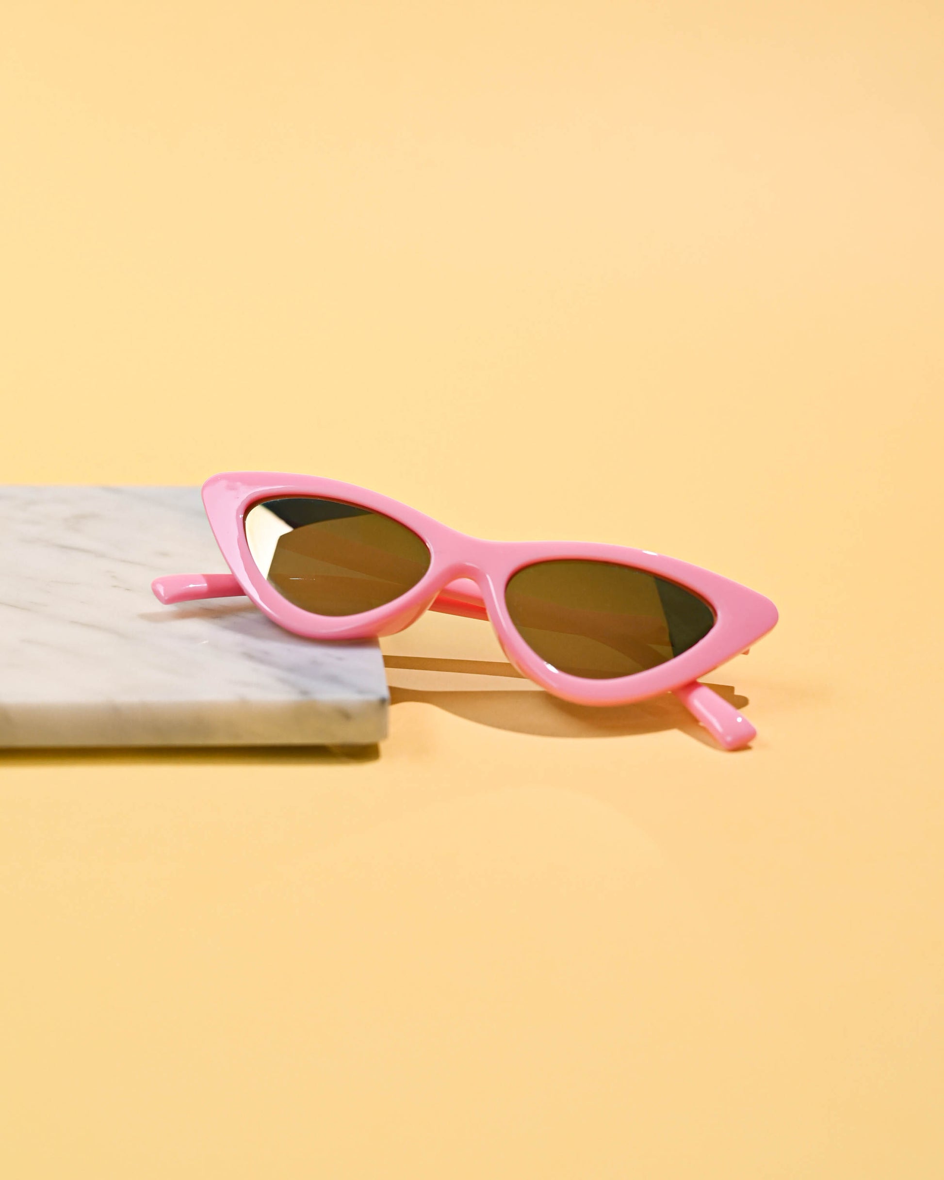 Classic pink cat-eye sunglasses resting on a marble and yellow dual-tone background, showcasing timeless style.