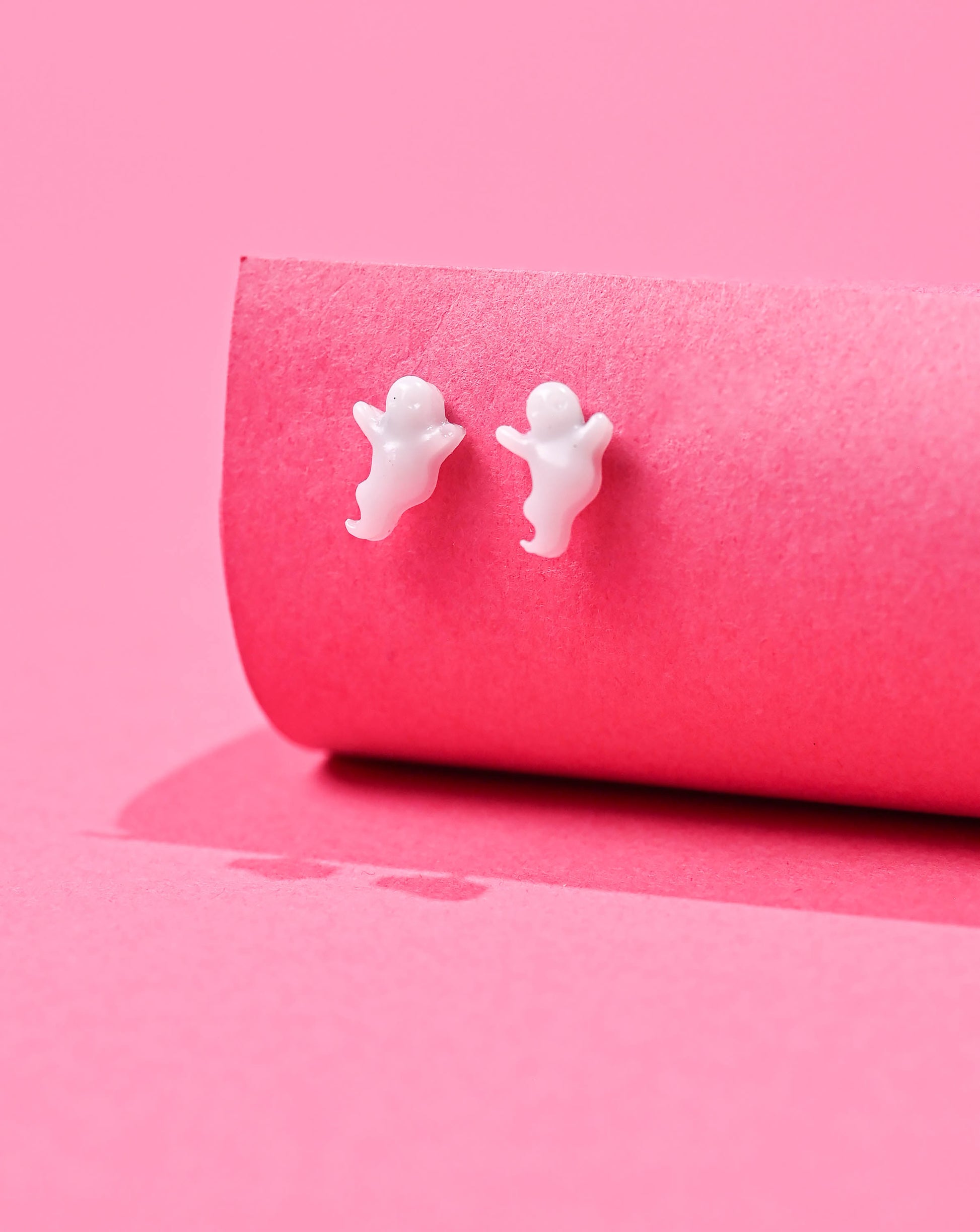 Whimsical white ghost stud earrings on a bright pink backdrop, ready to add a spooky yet cute charm to any look.