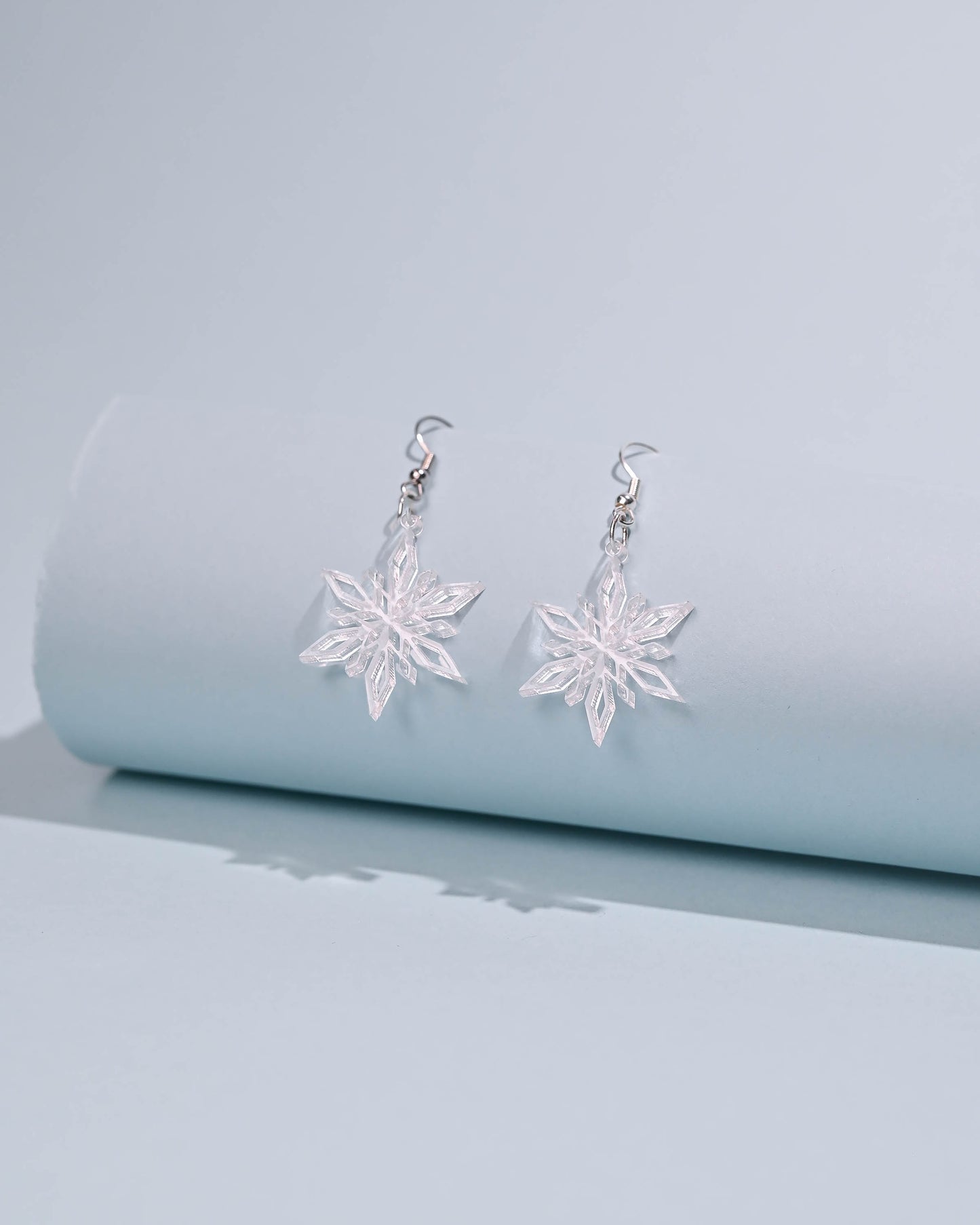 Clear snowflake dangle earrings on a white background, showcasing a delicate and transparent design.