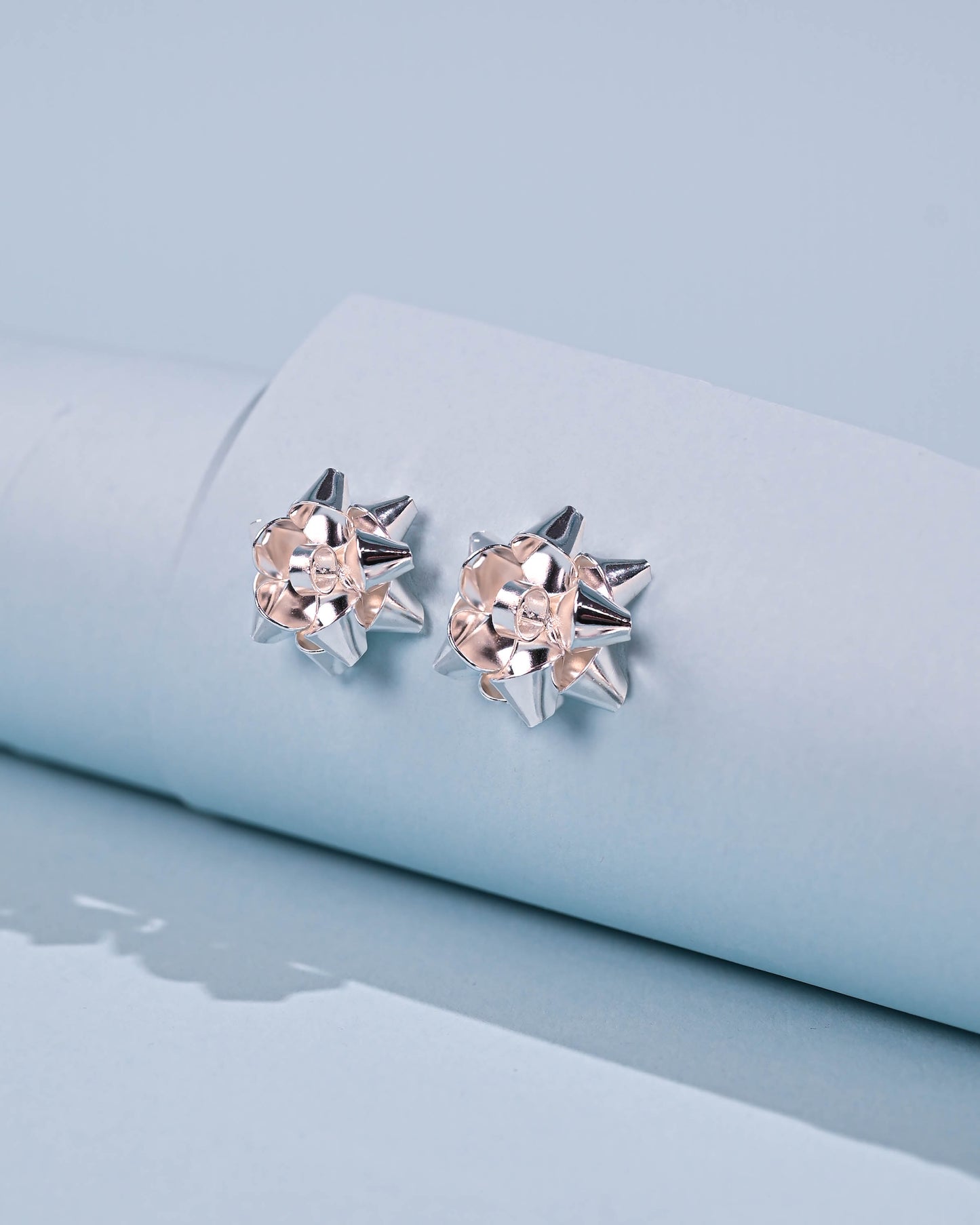 Silver Bow Earrings with a metallic finish on a light blue backdrop, exuding elegance and charm