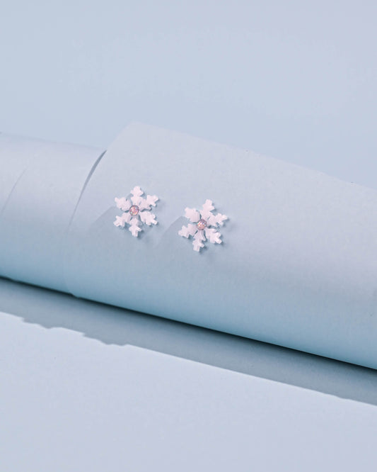 Close-up of snowflake stud earrings on a soft blue background, showcasing the white resin detail and stainless steel construction.