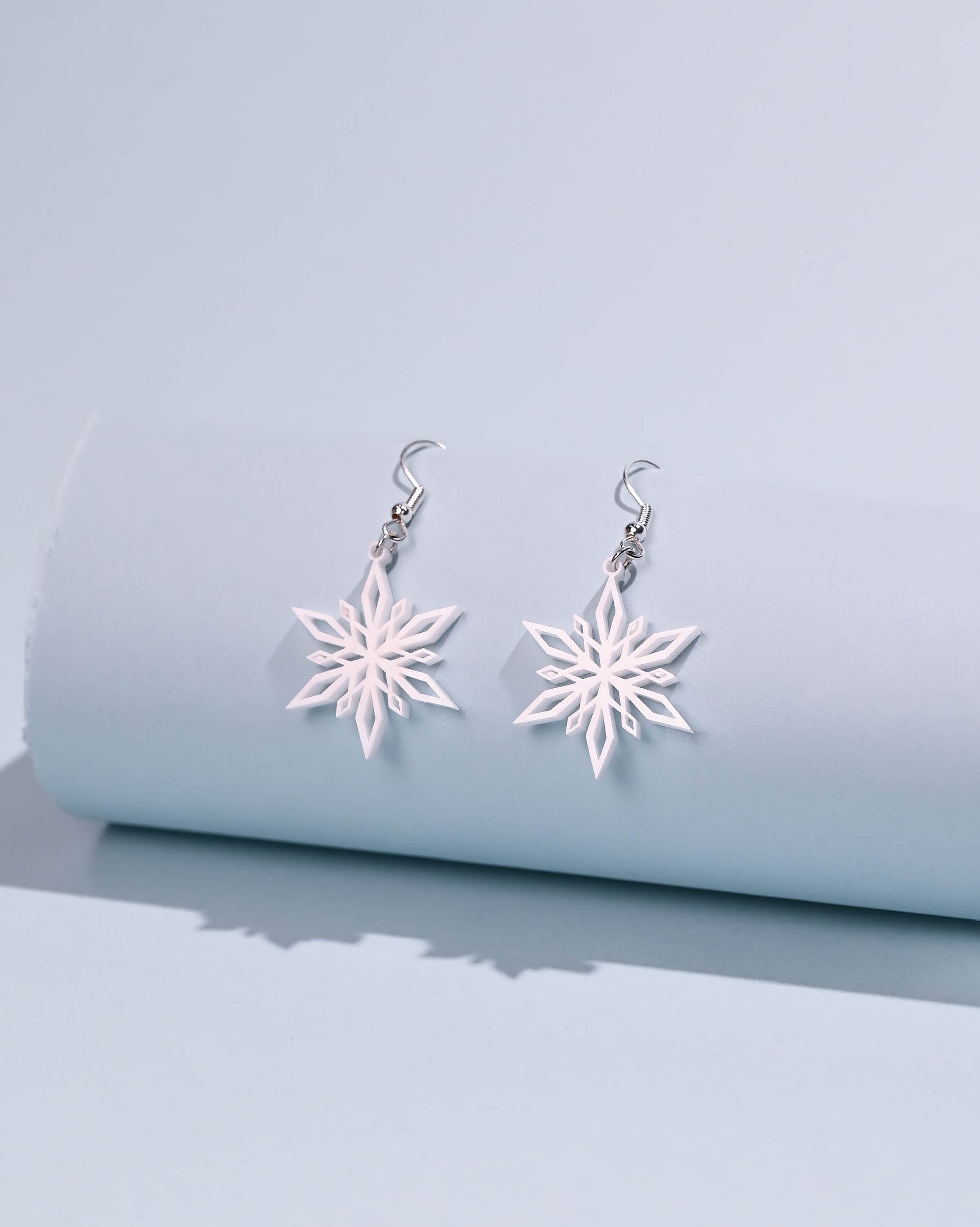 White snowflake dangle earrings with a soft focus on a neutral background, highlighting their intricate pattern.