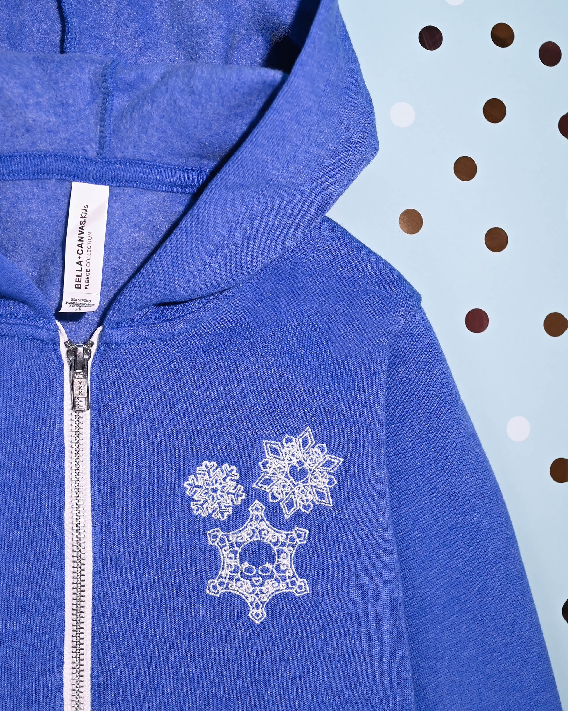 Close-up of blue hoodie with detailed snowflake and skull embroidery, perfect for a unique winter style.