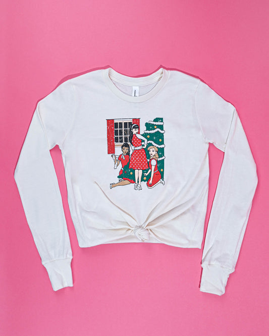 Festive long-sleeved white Christmas Trio Tee with a holiday tree graphic, laid flat against a vibrant pink background for a cheerful display.