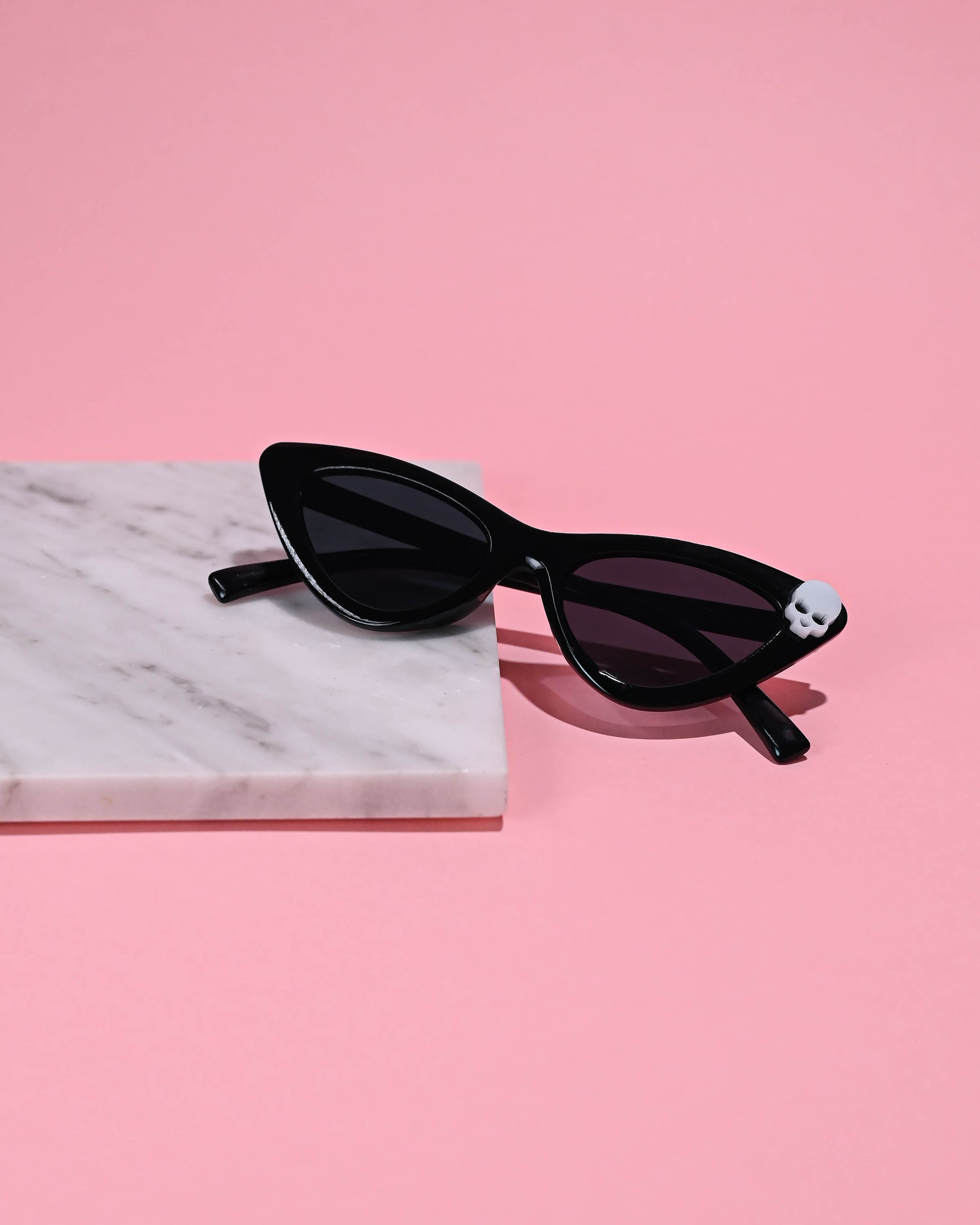 Black Skull Cat Eye Sunglasses placed against a pink backdrop, radiating a cool, retro vibe.