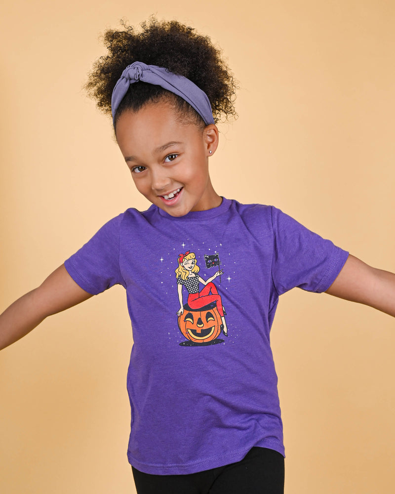 Girl smiling in a purple Black Cat Masquerade Tee with a comfortable fit and festive graphic print, paired with a light purple headband. Ideal Halloween shirt for girls.