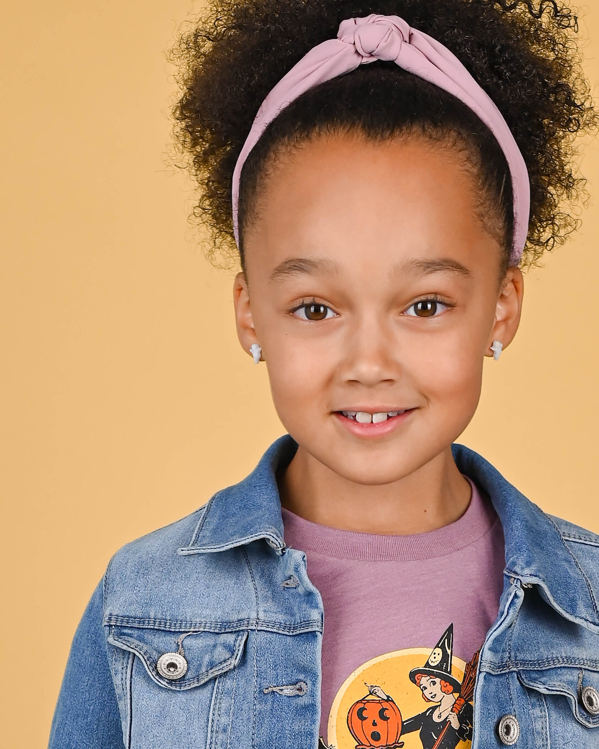 Joyful girl wearing white ghost earrings with a pink headband and denim jacket, exuding a playful and spirited fashion sense.