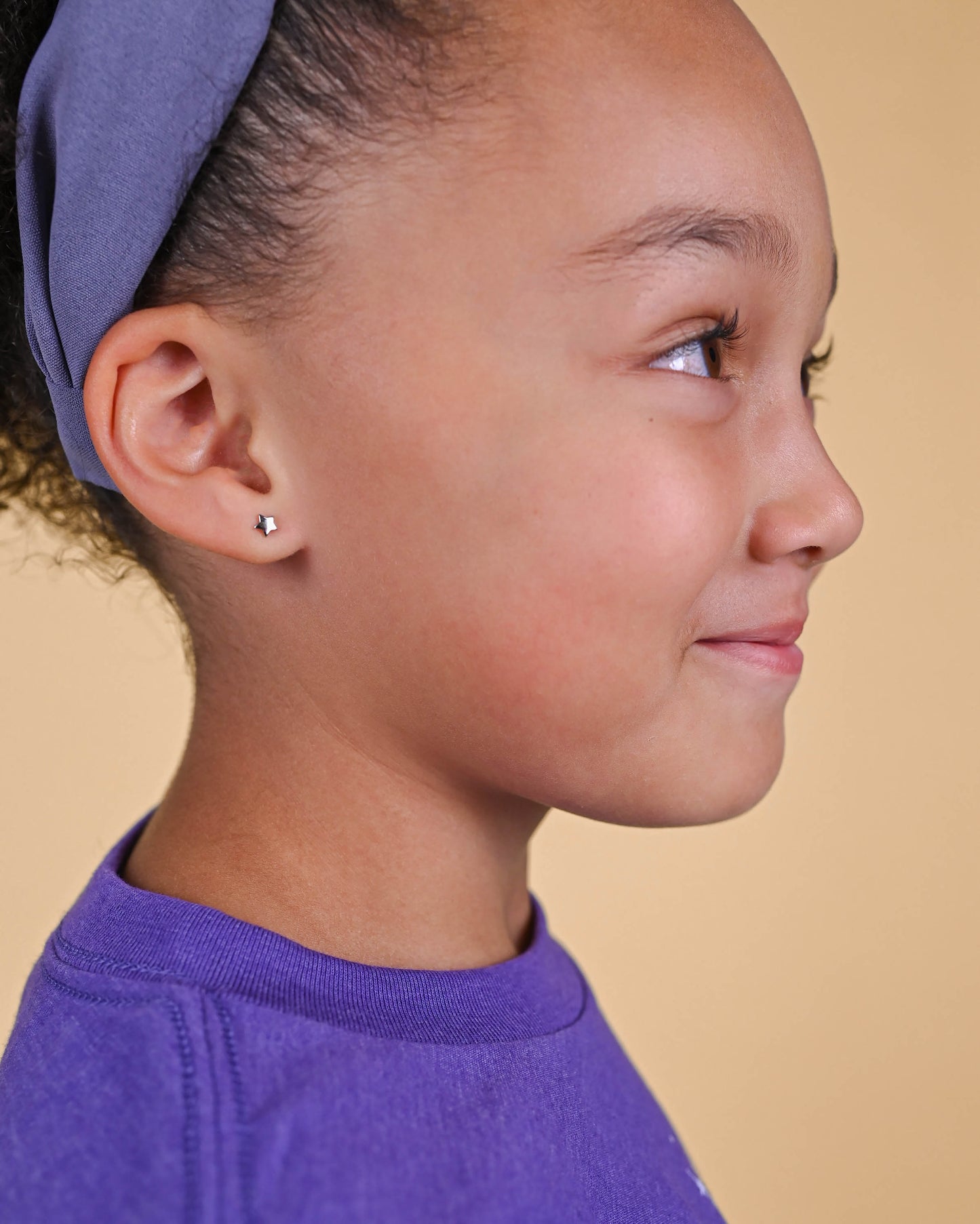 A young girl's ear adorned with a delicate Silver Star Stud Earring, capturing a touch of whimsy and sparkle.