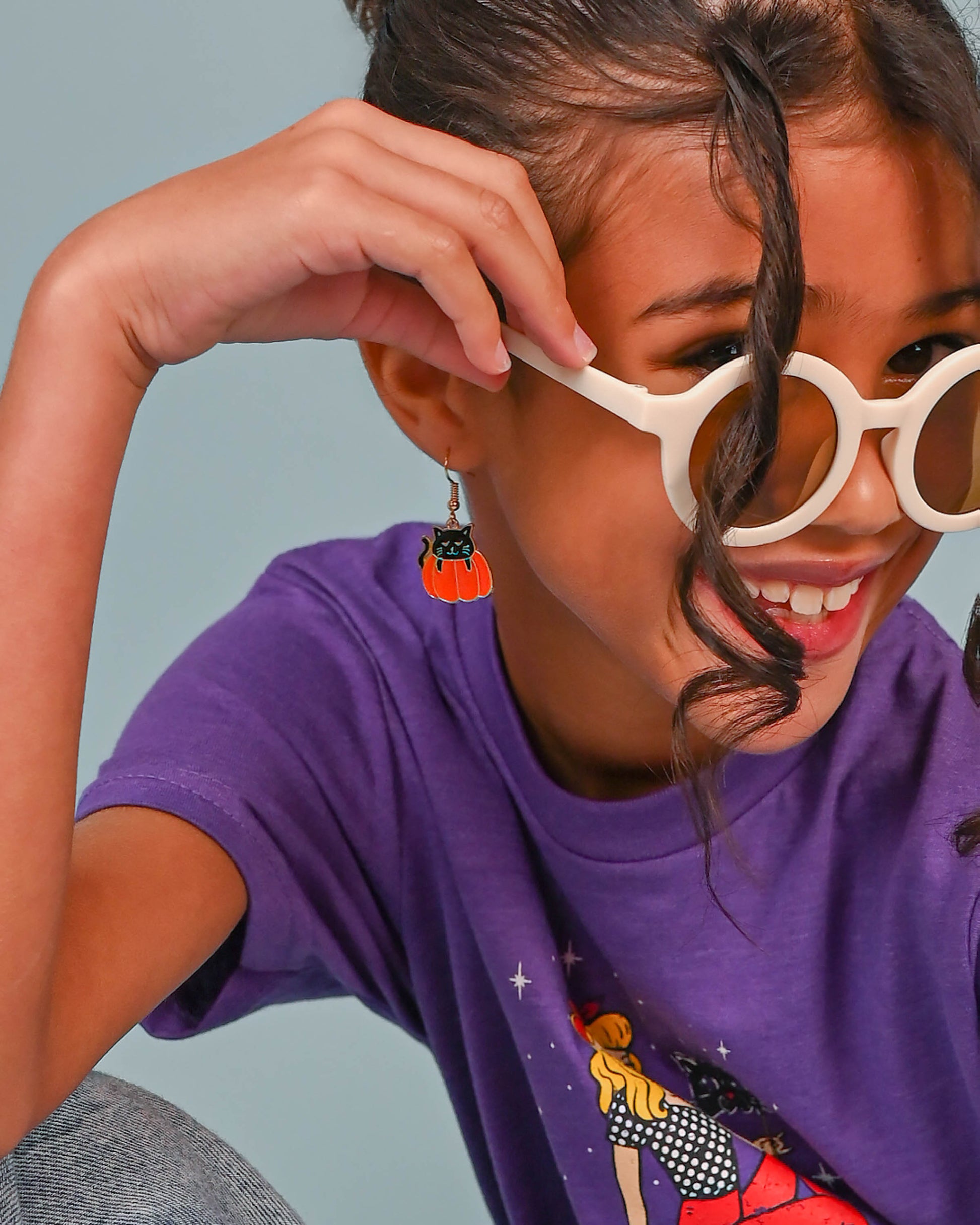 Cheerful girl wearing Black Cat Dangle Earrings, complementing her purple tee and white round sunglasses.