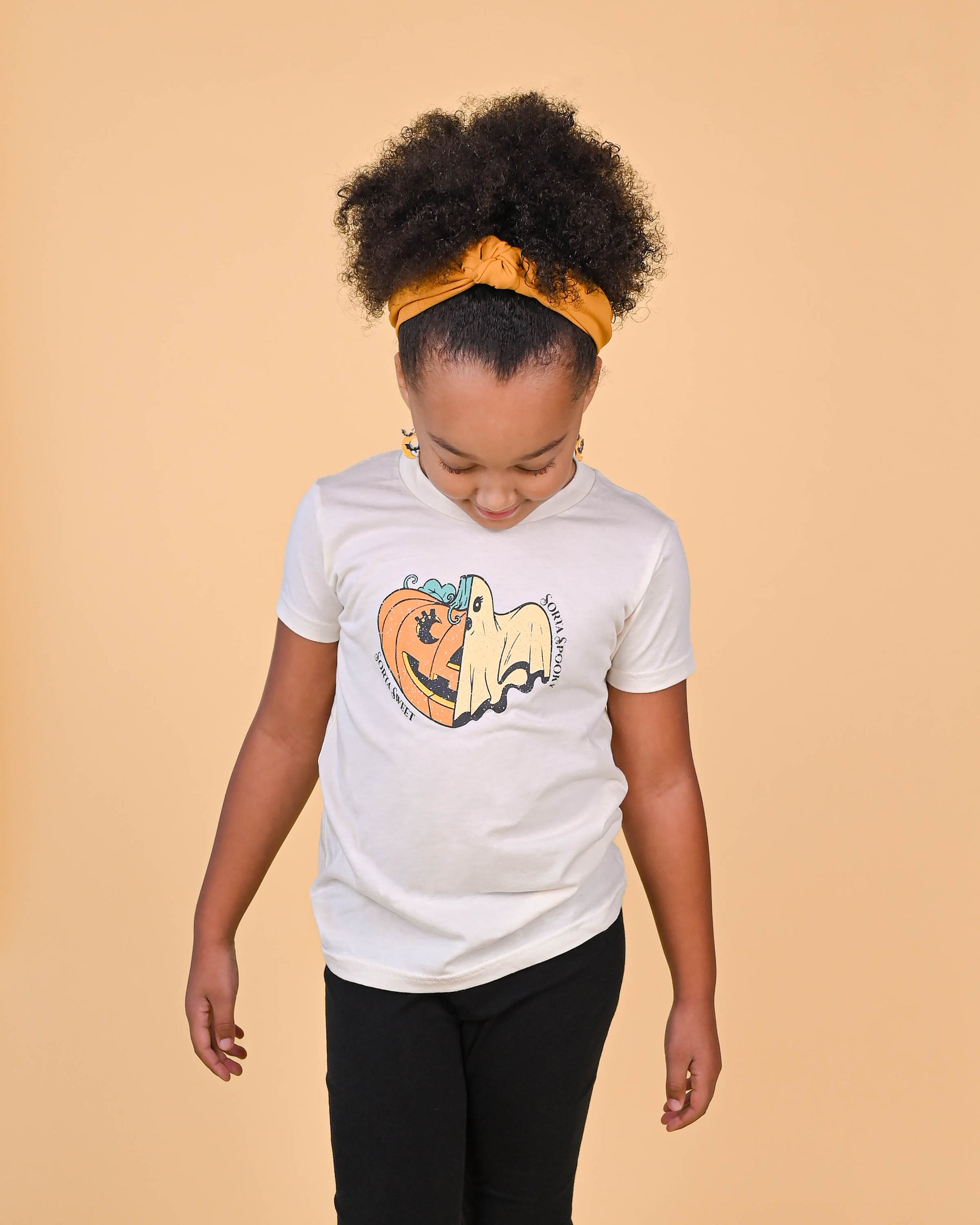 Young girl smiling wearing the 'Sorta Sweet Sorta Spooky' t-shirt, pairing it with a bright headband.