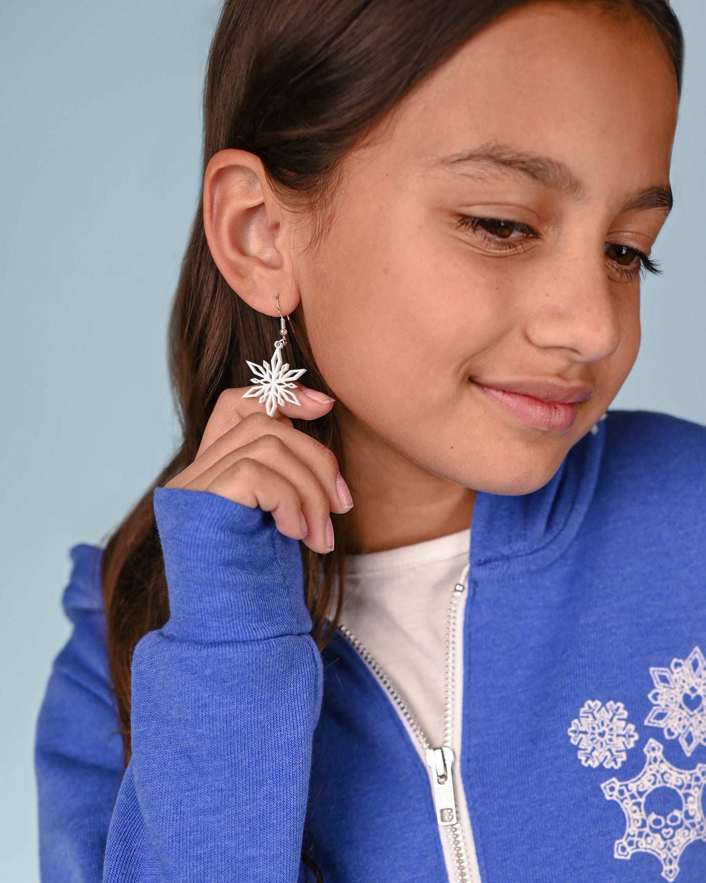 Close-up of a young girl's ear showing off the white snowflake earring, paired with a festive outfit.