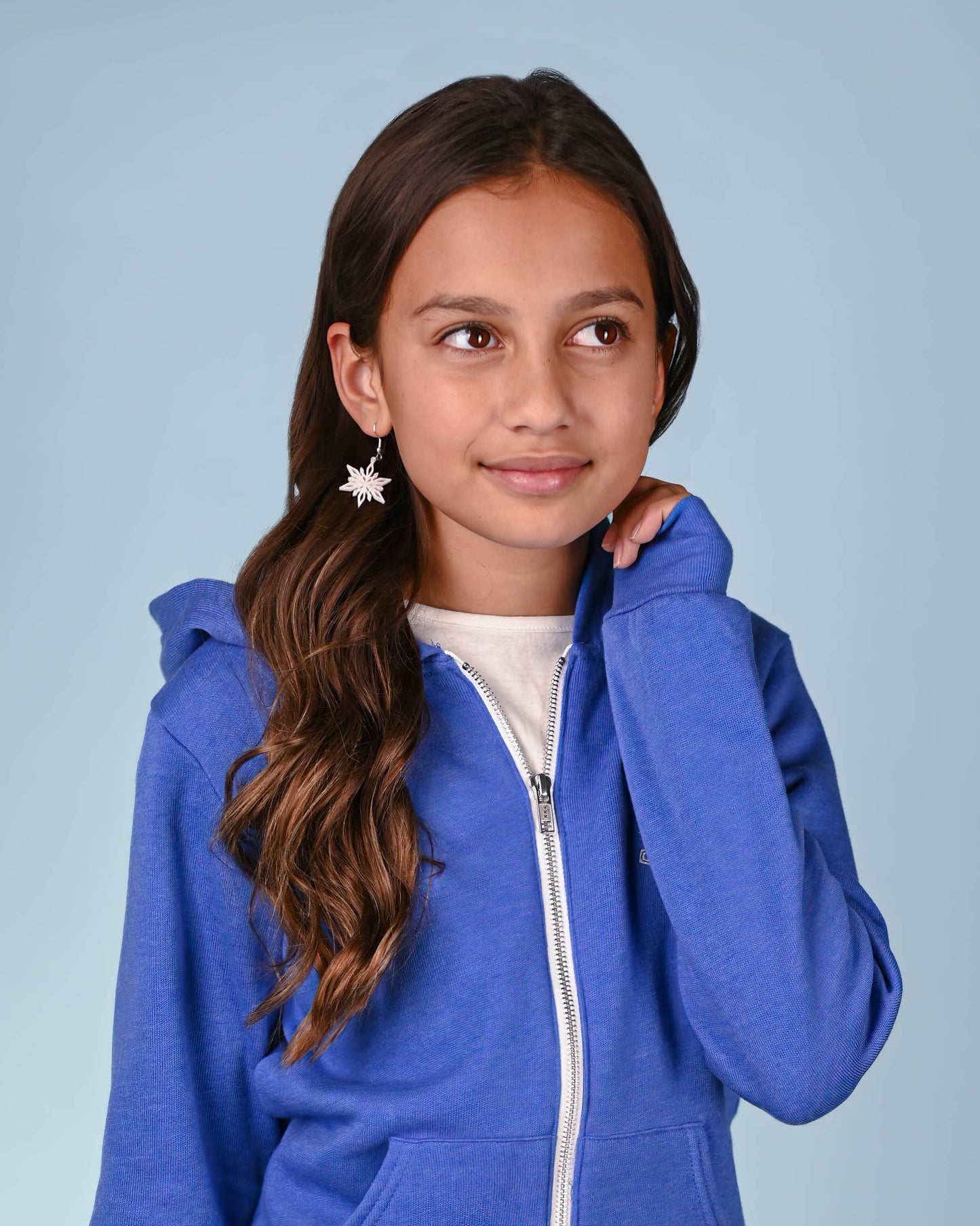Young girl smiling, wearing white snowflake dangle earrings, complementing her casual blue hoodie.