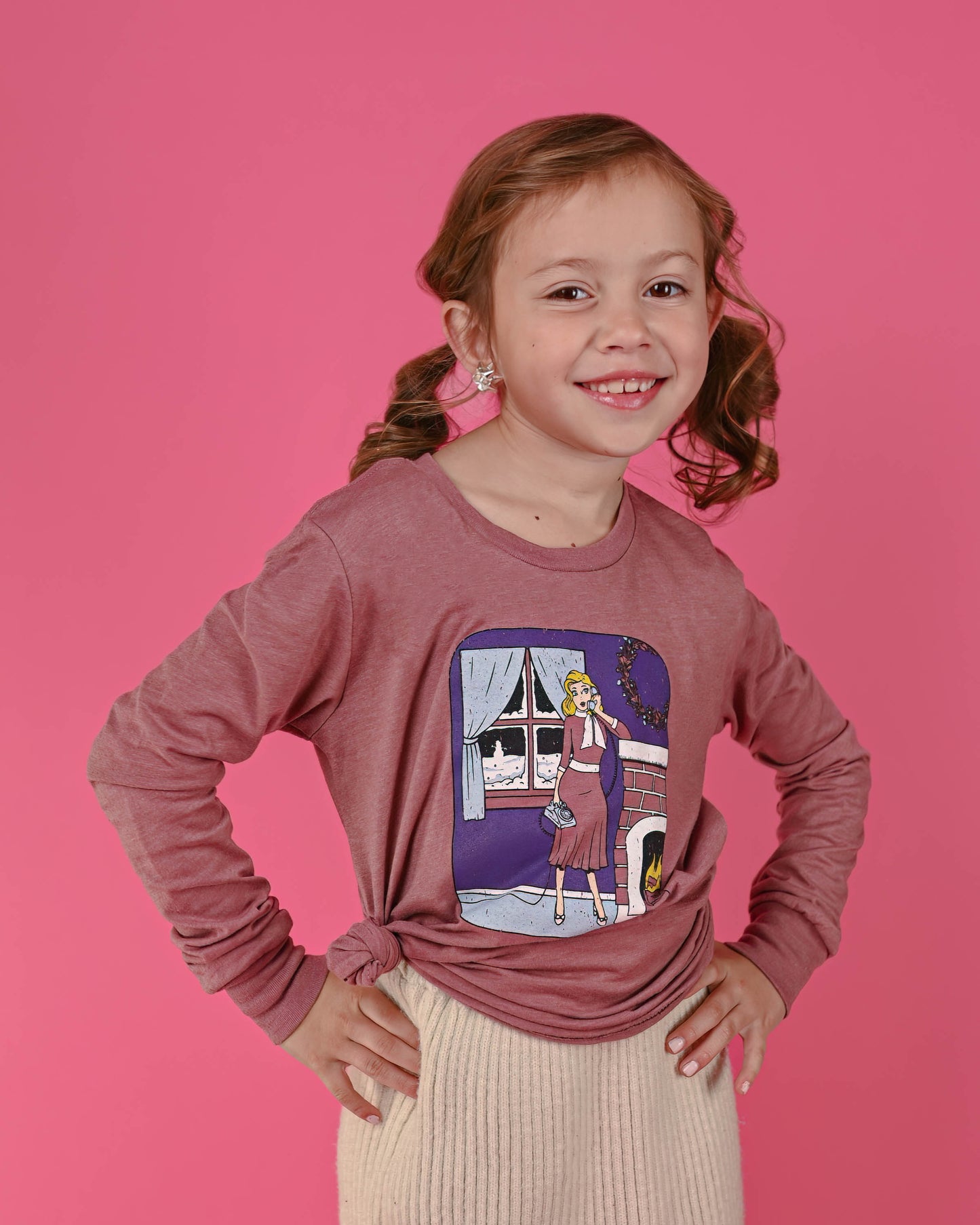 Happy young girl in a Gossip Girl long sleeve tee in mauve, with a vintage phone print, looking cheerful against a pink background.