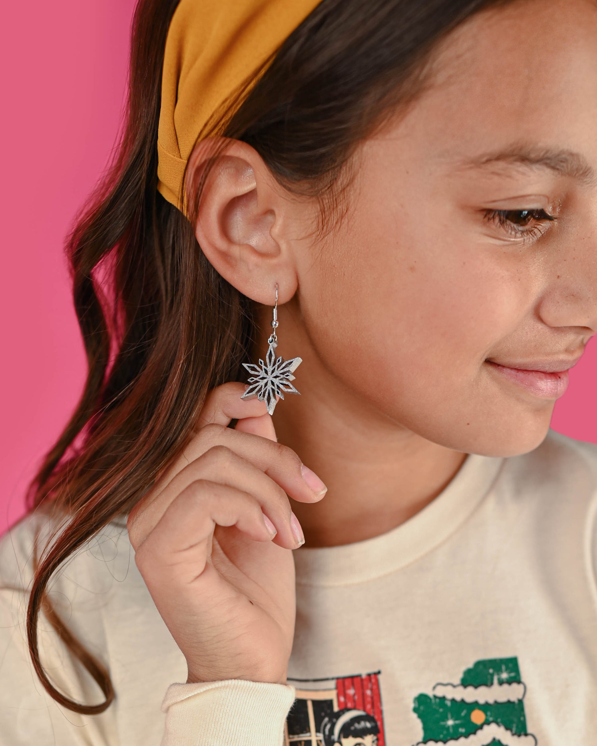 Silver snowflake dangle earrings displayed against a soft pink backdrop, emphasizing their shiny metallic finish.